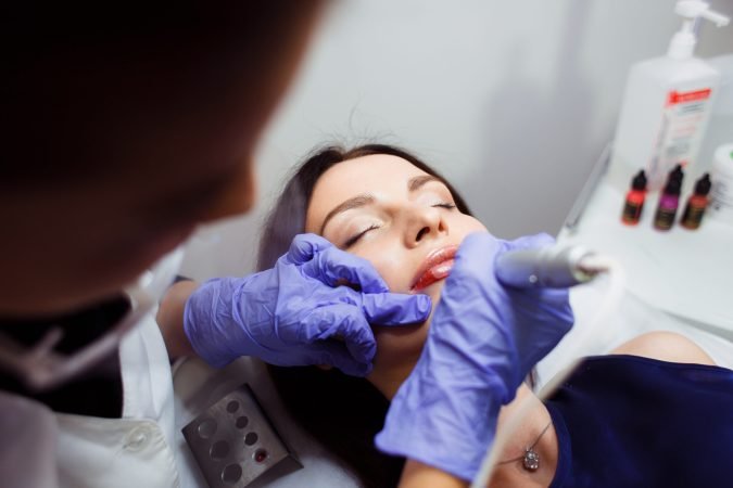 Young woman having permanent makeup on lips in beautician salon. Close up