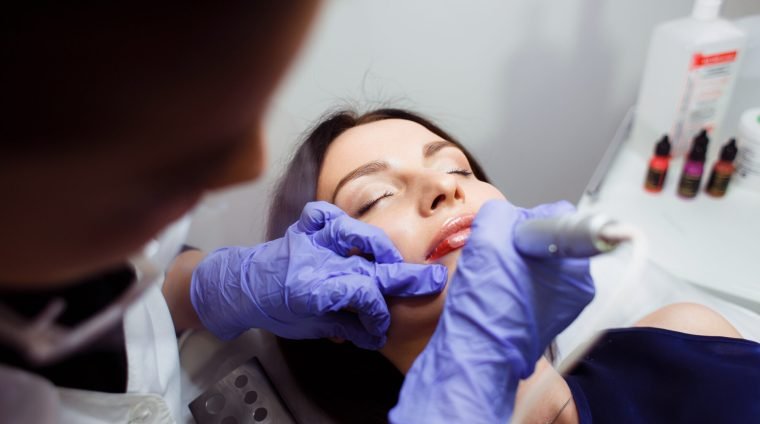 Young woman having permanent makeup on lips in beautician salon. Close up